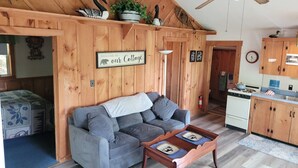 A cozy cabin-style room with a gray sofa, a wooden ceiling, and a kitchenette. - Treehouse type cottage in private location - Pet friendly! (Franklin)