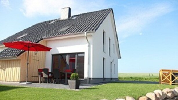 A house with a sloped roof, a red umbrella, and a stone wall in the foreground. - Ferienhaus Thormarcon (Goehren-Lebbin)