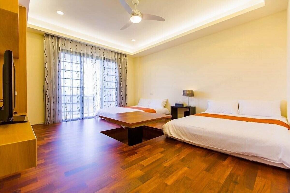 A hotel room with two beds, a flat-screen TV, a ceiling fan, and a large window with curtains.