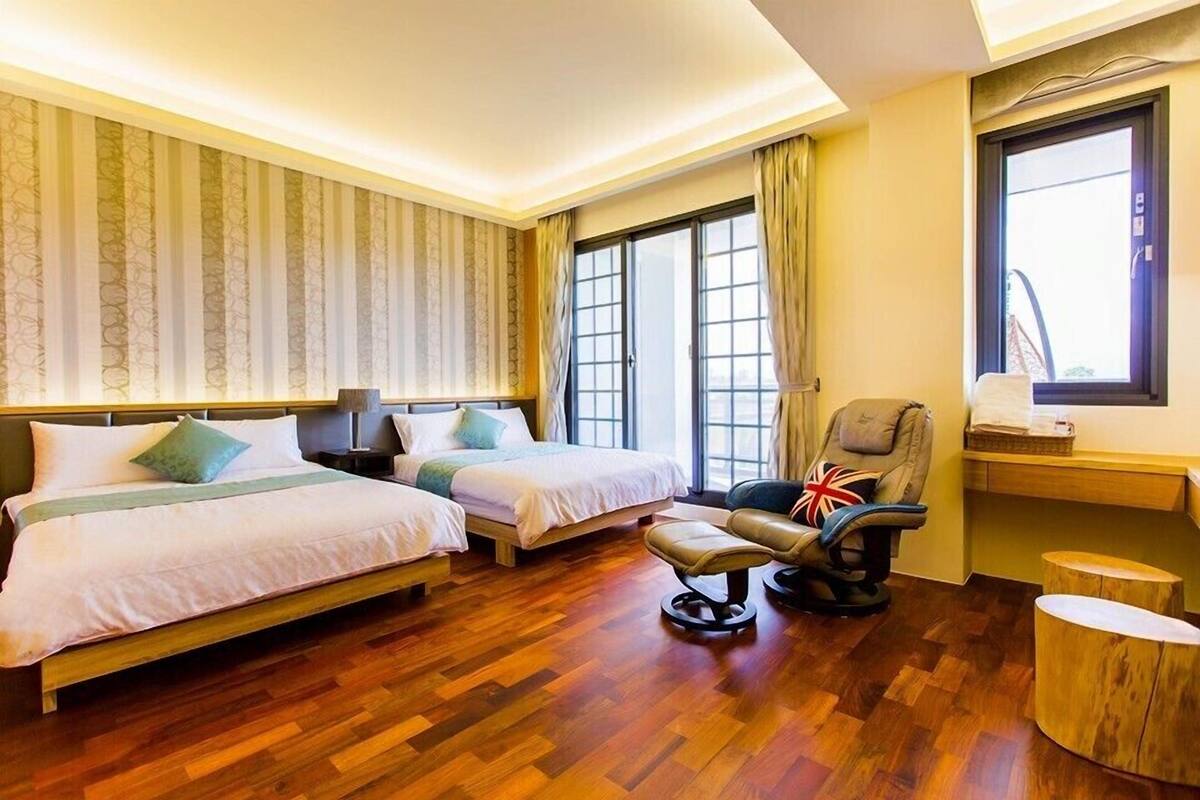 A hotel room with two beds, a chair, a small table, and a window with curtains.