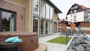 Un patio exterior moderno con un jacuzzi, zona de estar y vistas a un edificio de ladrillo con ventanas amplias.