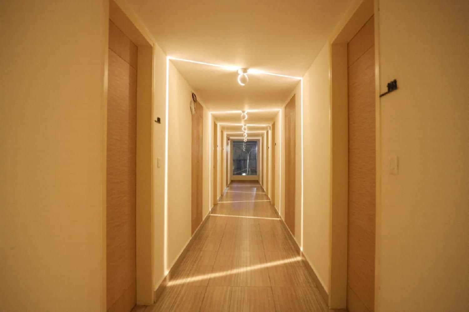 En hotellkorridor med trägolv, vita väggar och en taklampa.