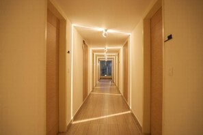 A hotel hallway with a wooden floor, white walls, and a ceiling light fixture. - First Inn Hotels (Chennai)