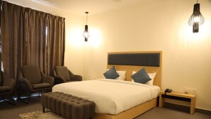 A modern bedroom with a large bed, two armchairs, a small bedside table, and a decorative rug.