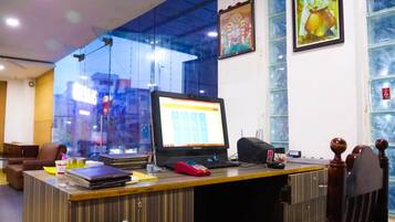 A reception desk with a computer monitor, a telephone, and a cash register. There are framed pictures on the wall and a window with a view of the city.