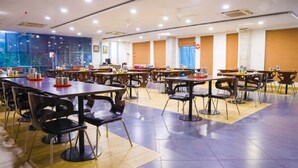 A spacious dining area with multiple tables and chairs, large windows, and a modern interior design.