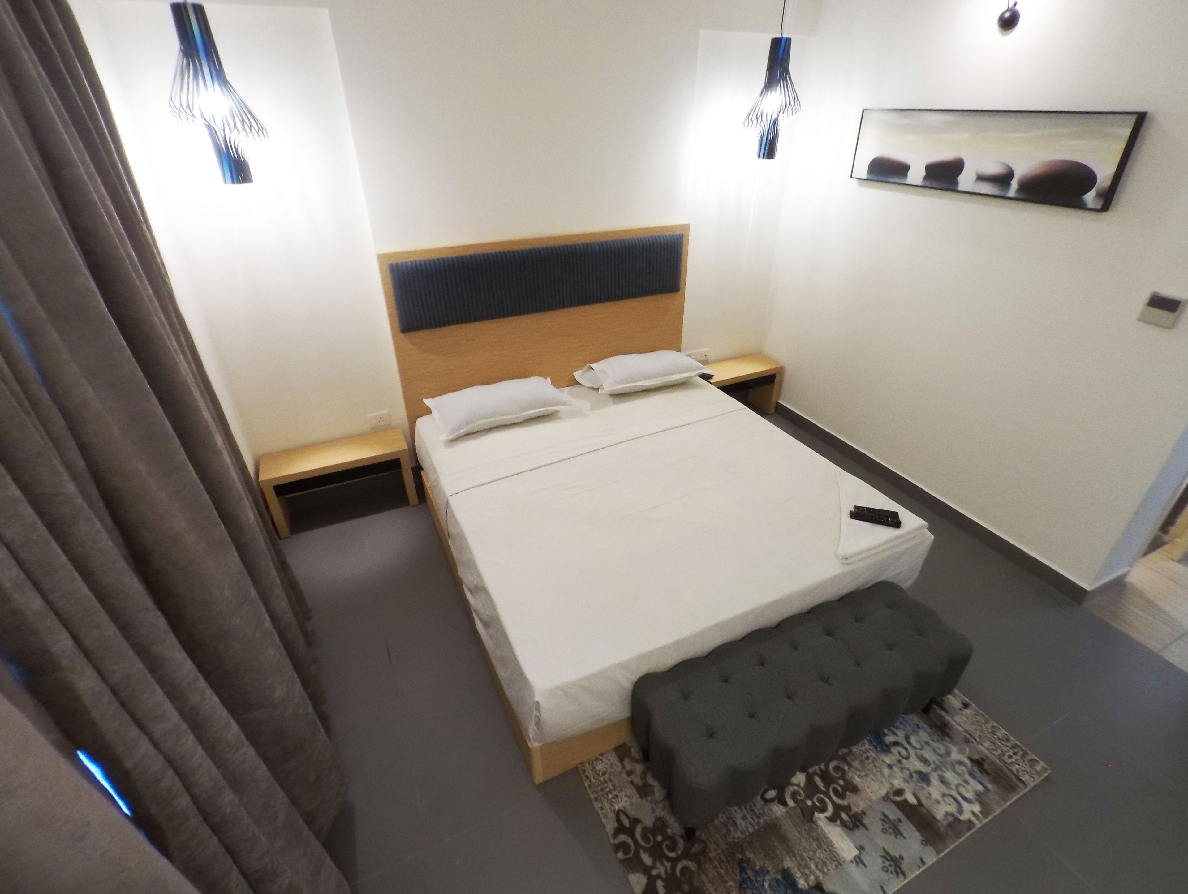 A modern hotel room with a large bed, bedside tables, a bench, and a patterned rug.