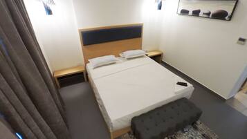 A modern hotel room with a large bed, bedside tables, a bench, and a patterned rug.