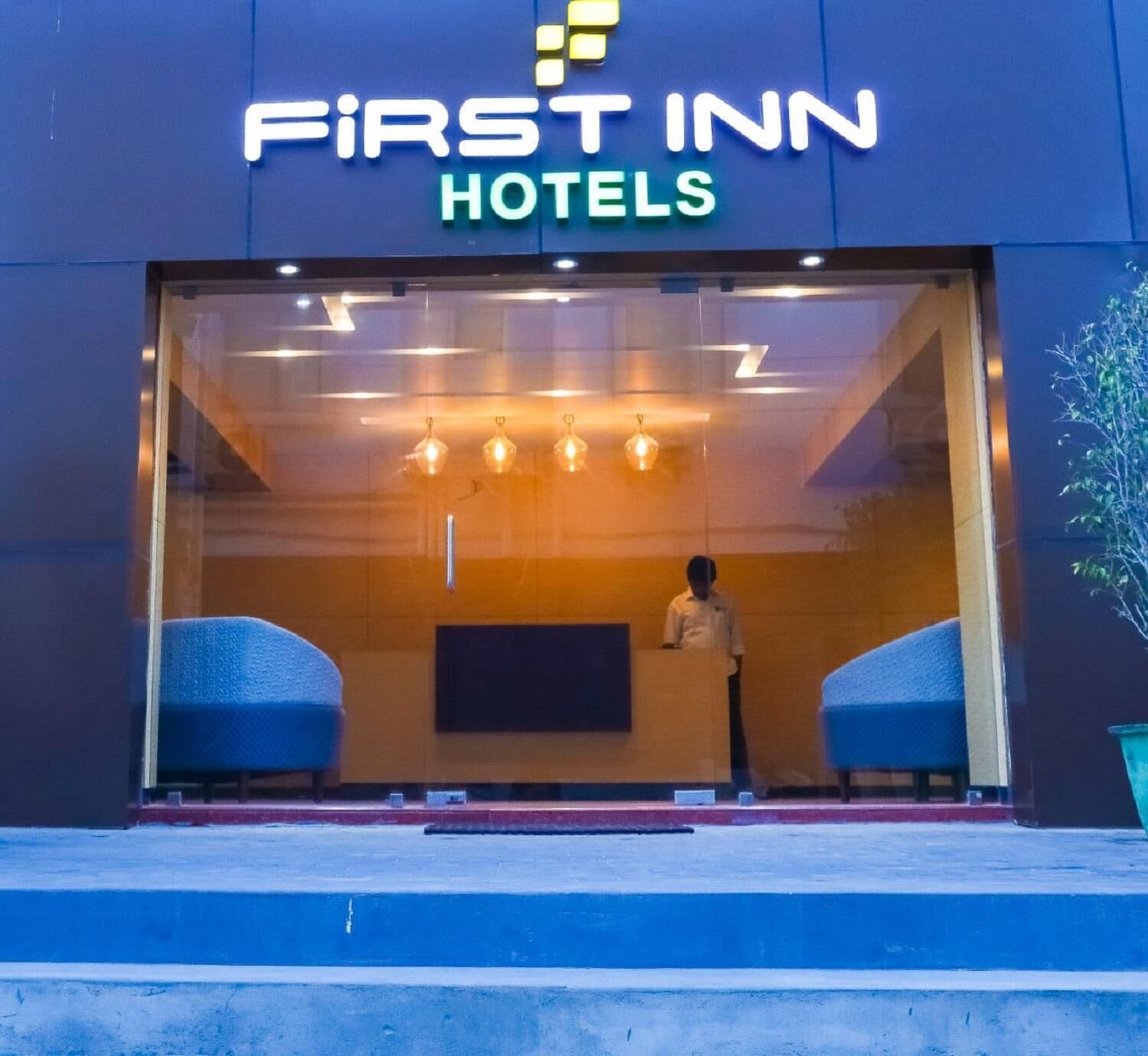 Entrada de un hotel con mostrador de recepción, dos zonas de estar y un ventanal grande.