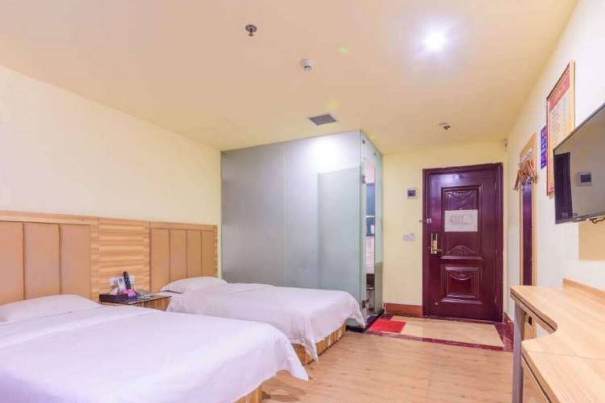 A hotel room with two beds, a wooden headboard, a flat-screen TV, and a wooden dresser.