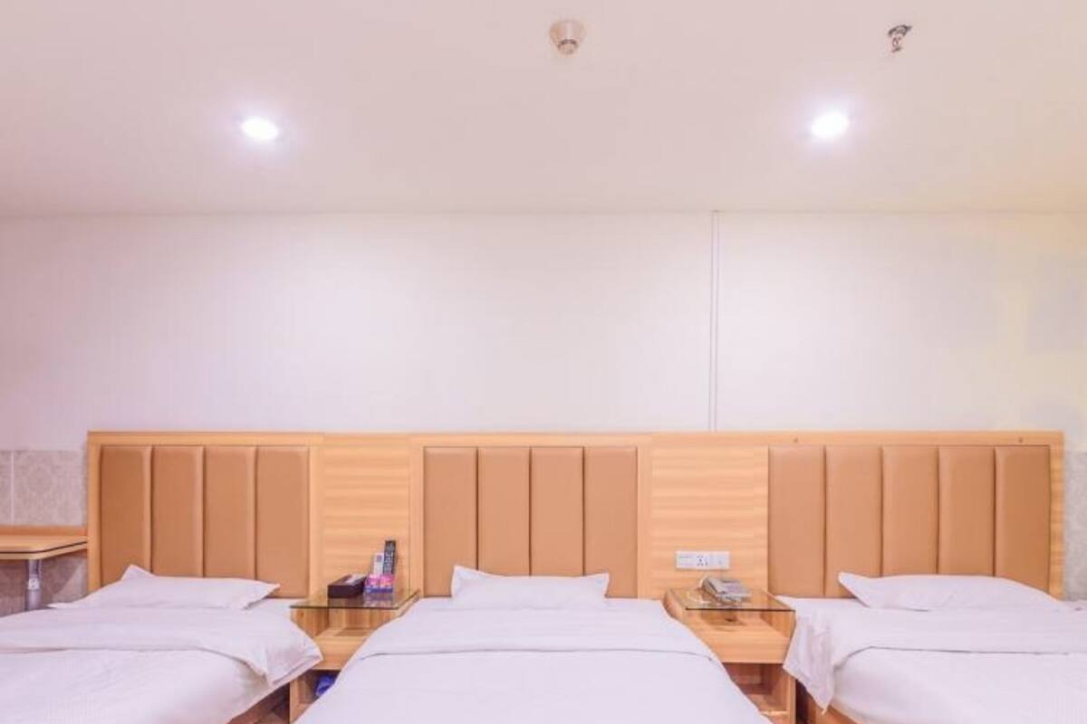 A hotel room with three single beds, wooden headboards, and bedside tables with lamps.