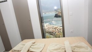 A room with a bed, towels, and a view of a coastal area with boats and rocky terrain. - Villa Maria Sea View by Estia (Mylopotamos)