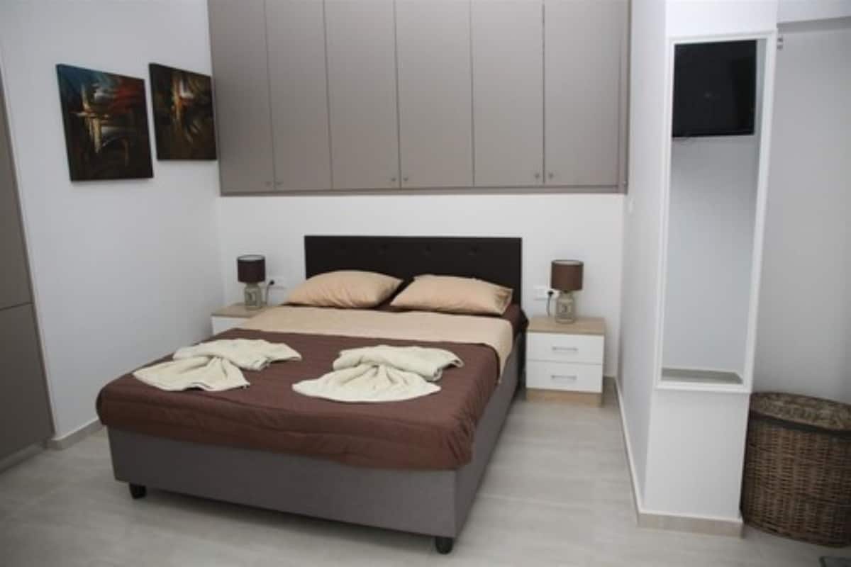 Une chambre à coucher avec un lit, des tables de chevet, une télévision et des œuvres d’art accrochées au mur.
