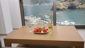 A dining table with a plate of watermelon and grapes, two glasses, and a bottle of wine, set against a scenic coastal view. - Villa Maria Sea View by Estia (Mylopotamos)