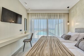 A modern hotel room with a large window, a flat-screen TV, a sofa, and a dining area.