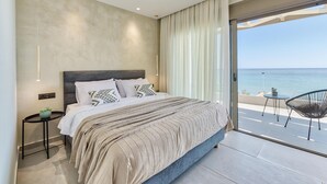 Un dormitorio con una cama grande, vistas al mar y un balcón con sillas.