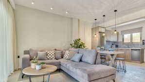 Una sala moderna con un sofá modular, una mesa de centro redonda y una cocina con mesa de comedor y taburetes de bar.