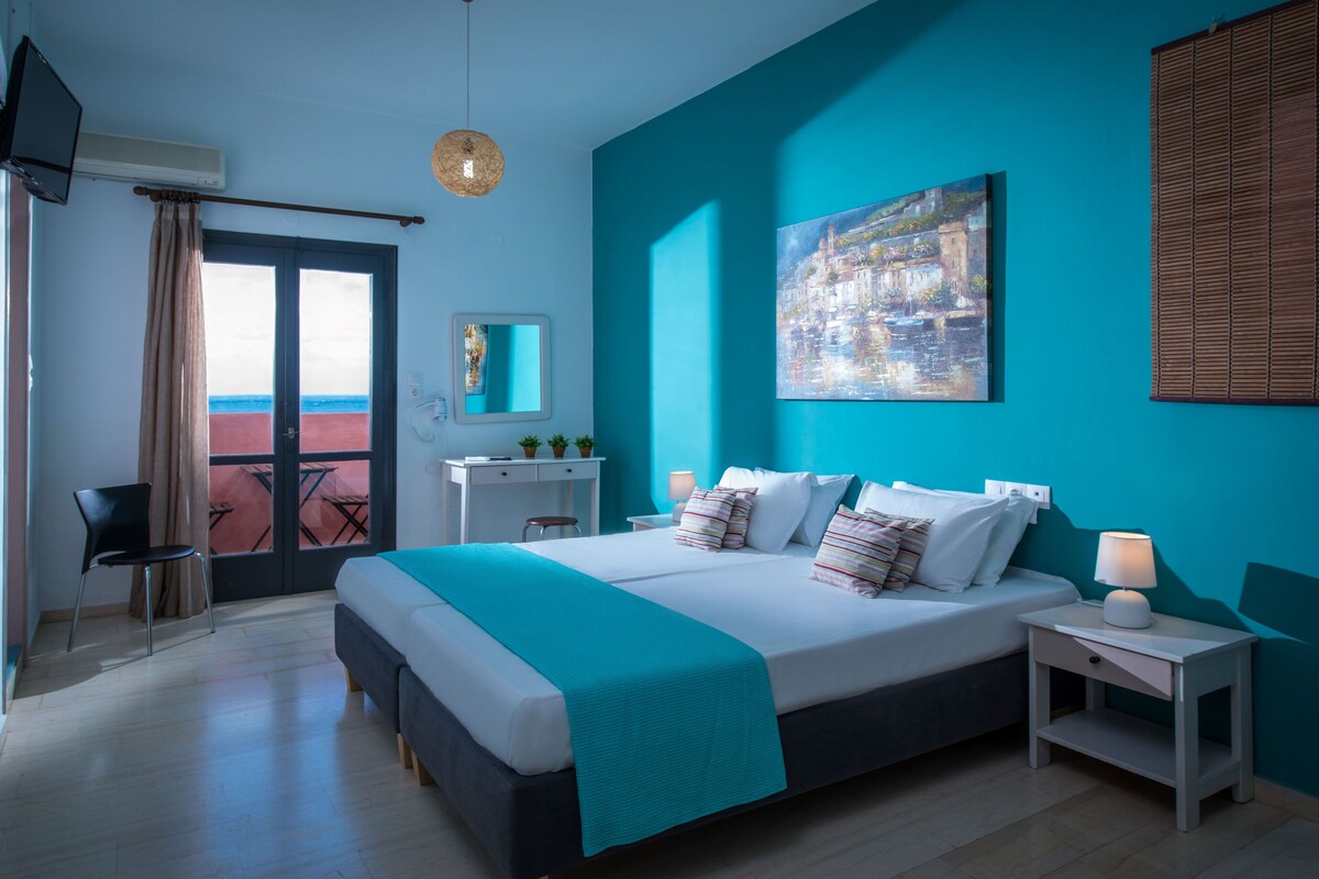 A hotel room with a bed, bedside tables, a desk, a chair, a window with curtains, and a painting on the wall.