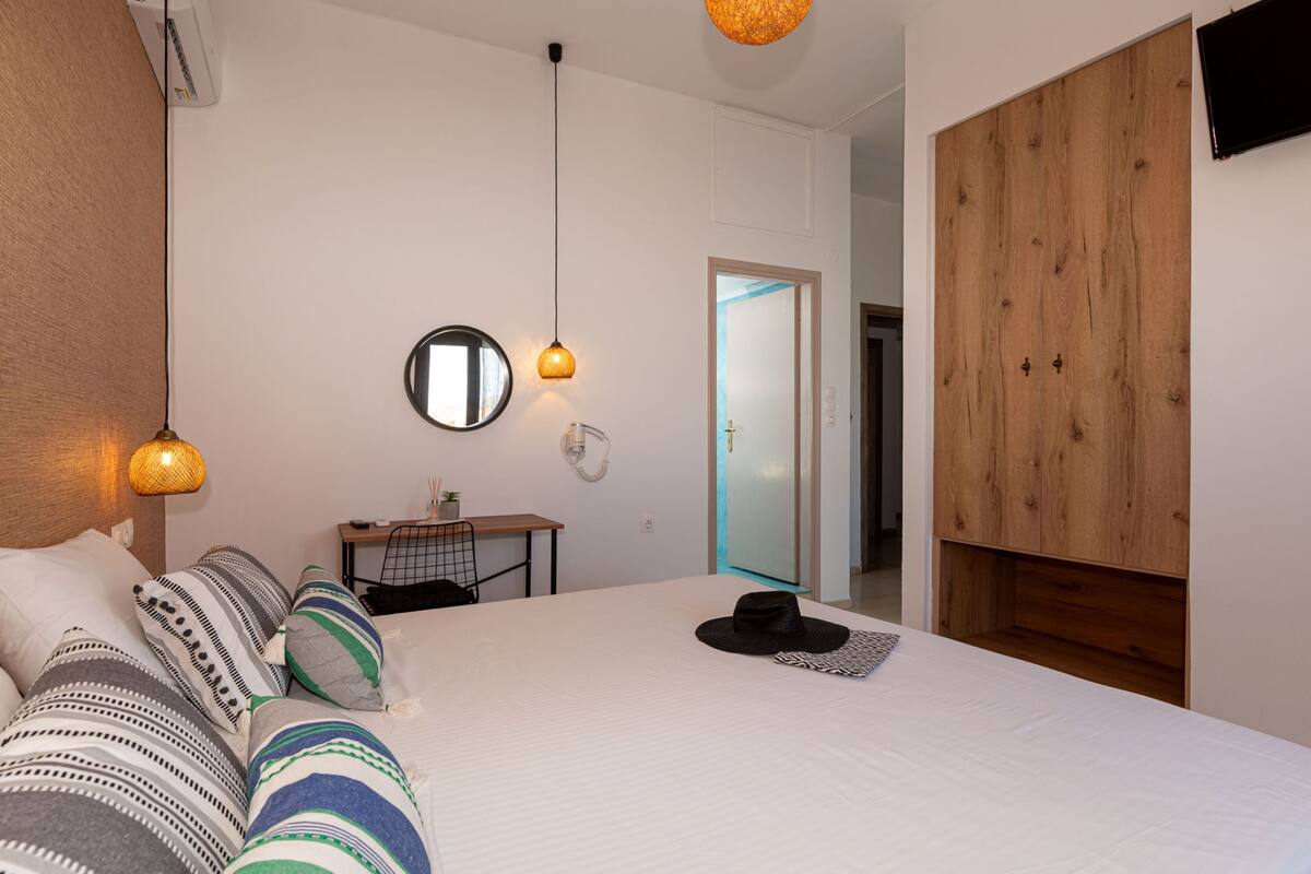 A bedroom with a large bed, a wooden wardrobe, a desk, and a mirror on the wall.