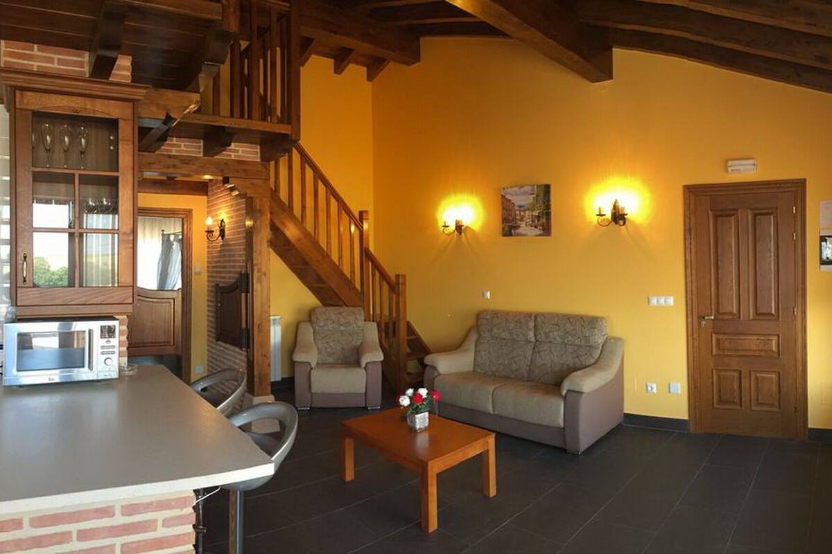 Ein Wohnzimmer mit einer Holztreppe, einer Sofagarnitur, einem Couchtisch und einer Küchenzeile mit einer Mikrowelle.