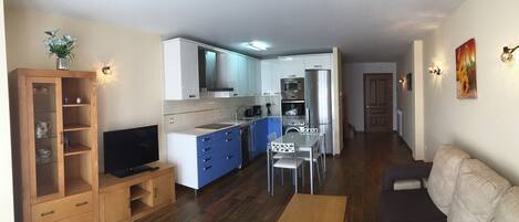 Un espacio habitable compacto con kitchenette, zona de comedor, televisor y sofá.