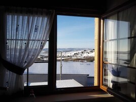 Quarto com uma grande janela que oferece vista para uma paisagem nevada e um edifício distante.