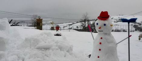 A snowman with a red hat and buttons, standing next to a fence in a snowy outdoor setting.