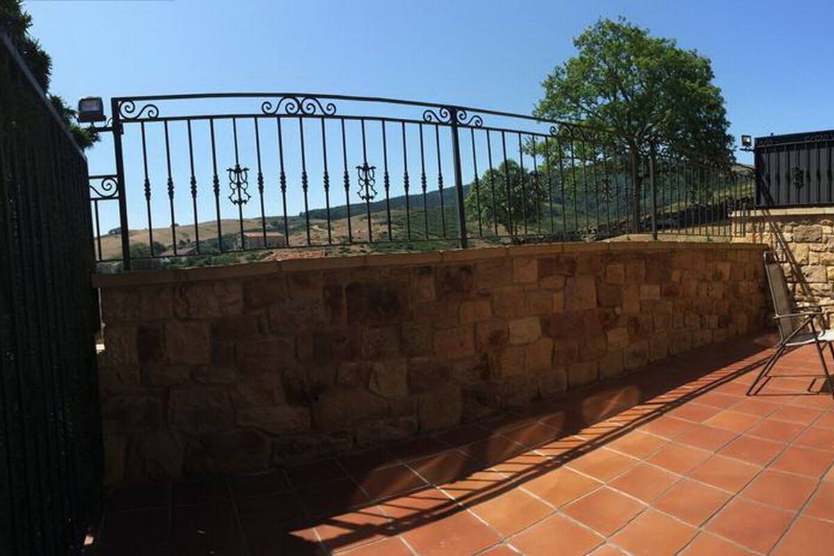 Eine Terrasse mit Steinmauern, einem Metallgitter und Gartenmöbeln.