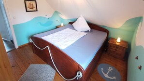 Une chambre à coucher avec un lit en bois, un oreiller blanc, une table de chevet avec une lampe et une fresque murale.