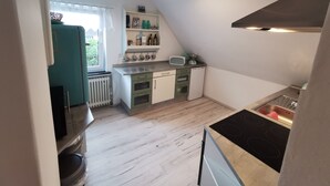 Une cuisine compacte dotée d’un four encastré, d’un évier et d’une fenêtre donnant sur un espace verdoyant.