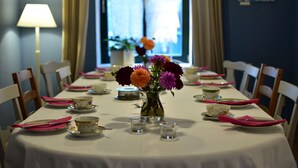 Een eettafel gedekt met roze servetten, borden en een vaas met bloemen.