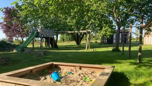 Een zandbak met zand en speelgoed, omringd door gras en bomen.