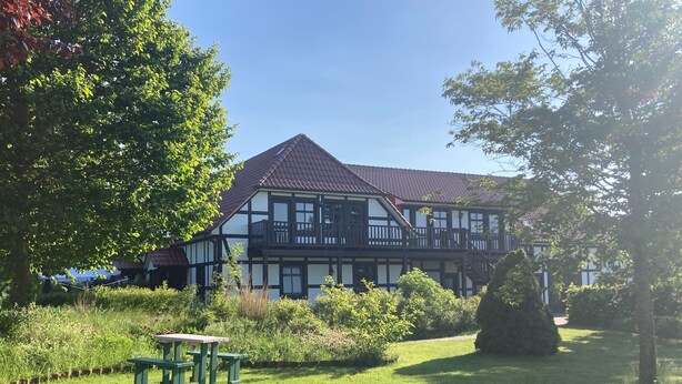 Een traditioneel vakwerkhuis met rode dakpannen, omgeven door een verzorgde tuin met een picknicktafel.