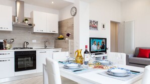 A modern kitchen with white cabinetry, a built-in oven, and a dining area with a white table set for four. - San Frediano Apartment (Florence)