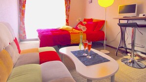 Hotellihuone, jossa on sänky, sohva, juomien kanssa tarjoiltava sohvapöytä, televisio ja ilmastointilaite.