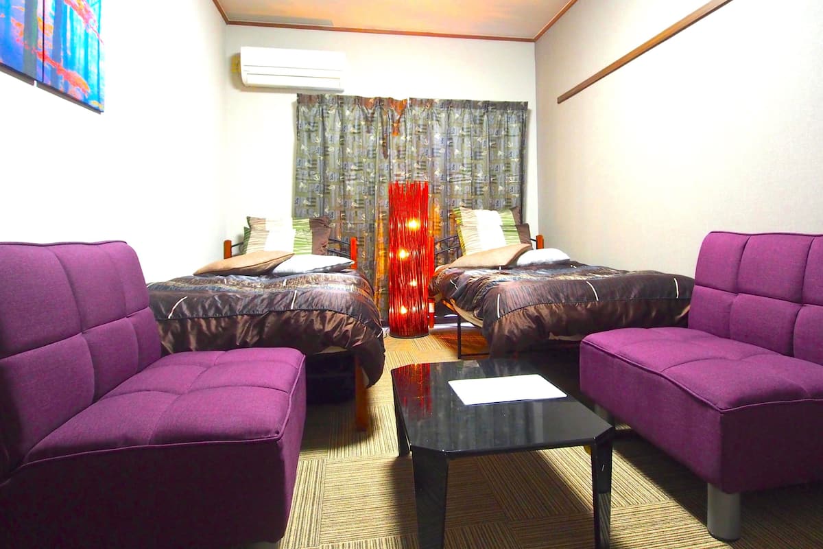A hotel room with two beds, a sofa, a coffee table, and an air conditioning unit.