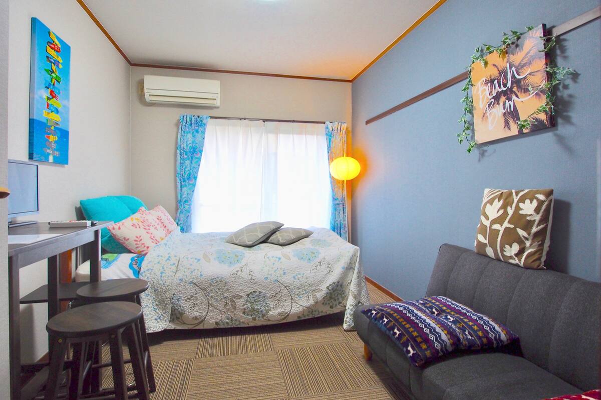 A bedroom with a bed, a desk, a chair, a sofa, and a lamp.