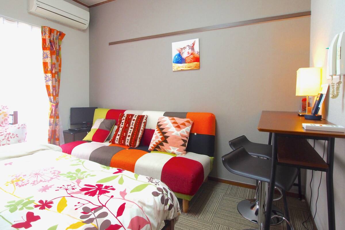 A hotel room with a bed, a desk, a chair, and a wall-mounted air conditioner.