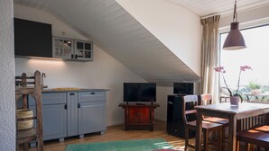 A kitchen with a TV, wooden furniture, and a dining area with chairs and a table. - Das Nest am Wohrenberg (Daisendorf)