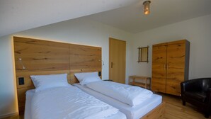 A bedroom with two single beds, wooden headboard, a wooden wardrobe, a small wooden table, and a black leather chair. - Das Nest am Wohrenberg (Daisendorf)