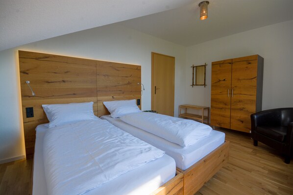 Un dormitorio con dos camas individuales, cabecero de madera, un armario de madera, una mesita pequeña de madera y una silla de cuero negro.