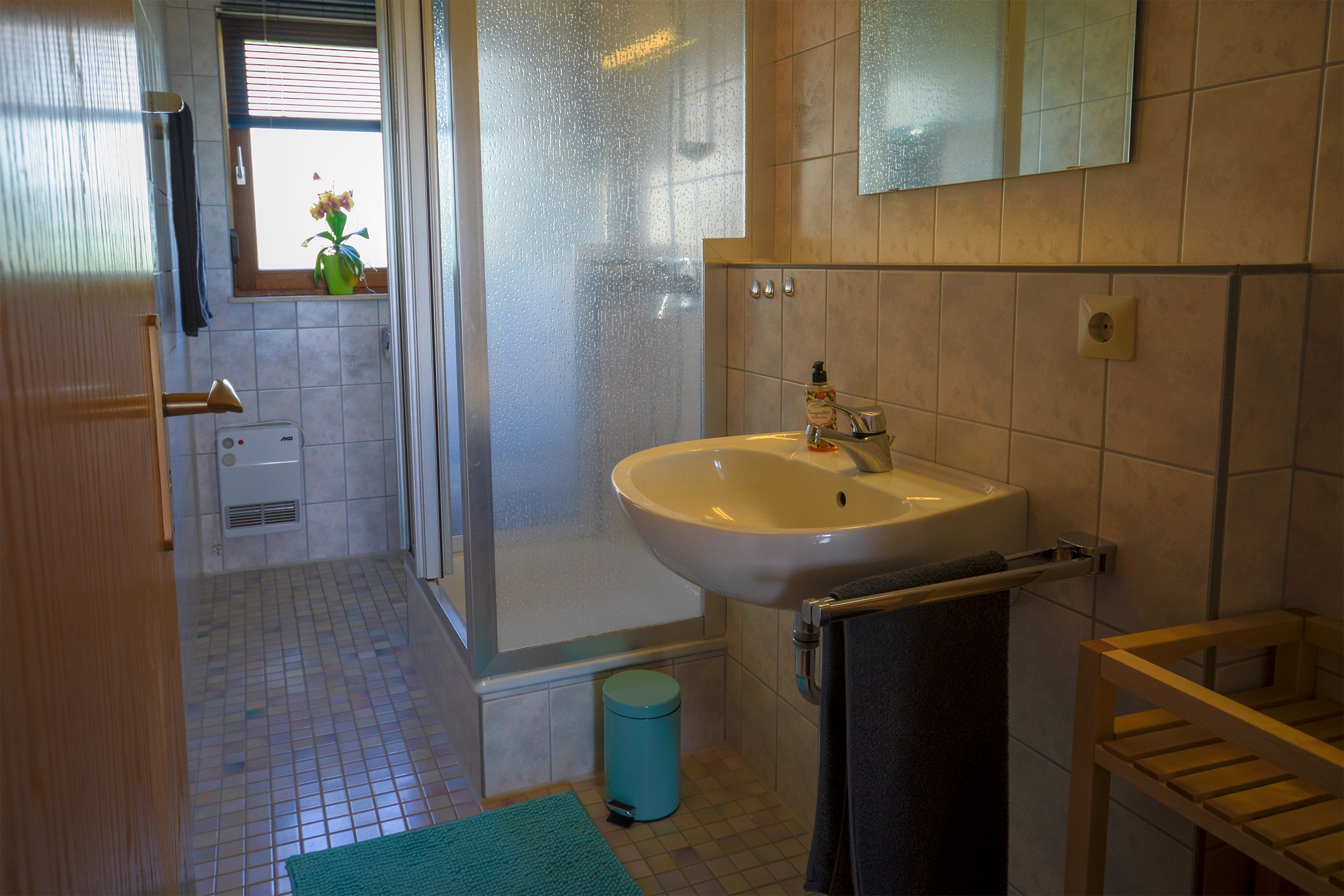 Une salle de bain avec une douche, un lavabo et une fenêtre agrémentée d’un vase de fleurs.