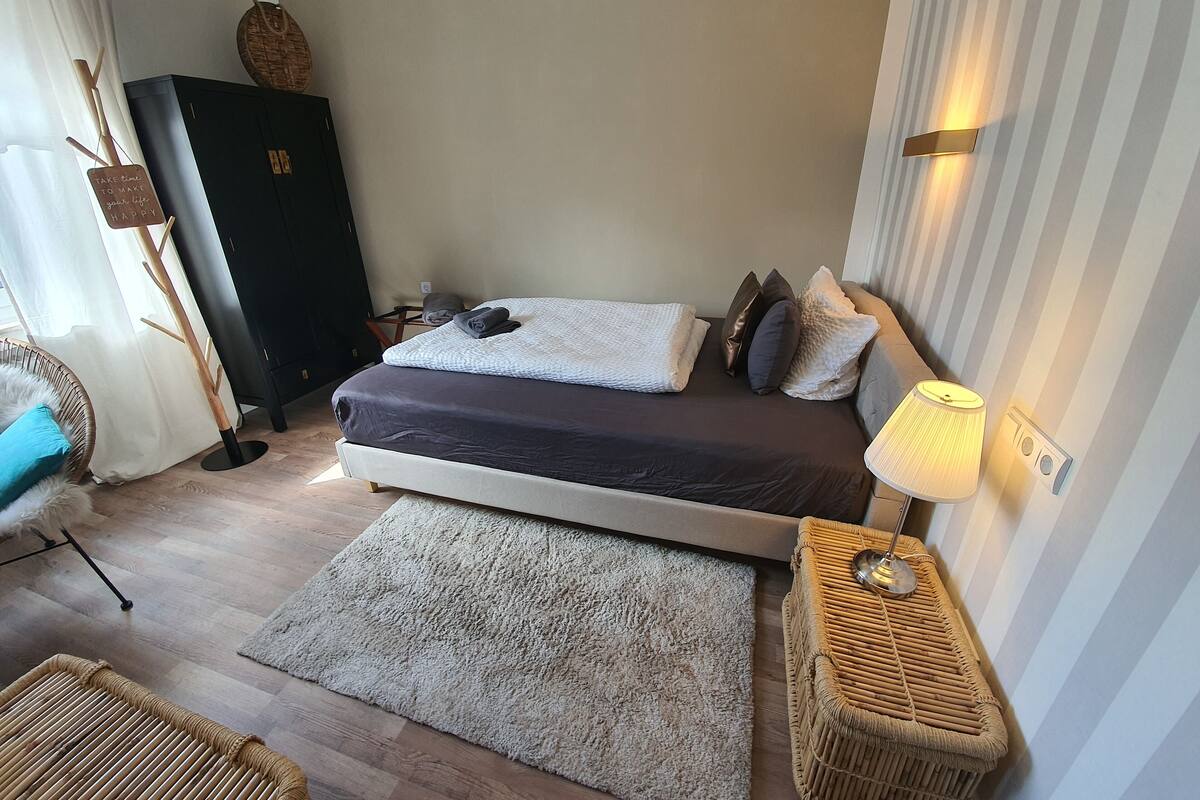 A modern bedroom with a bed, bedside lamp, and a large window with curtains.