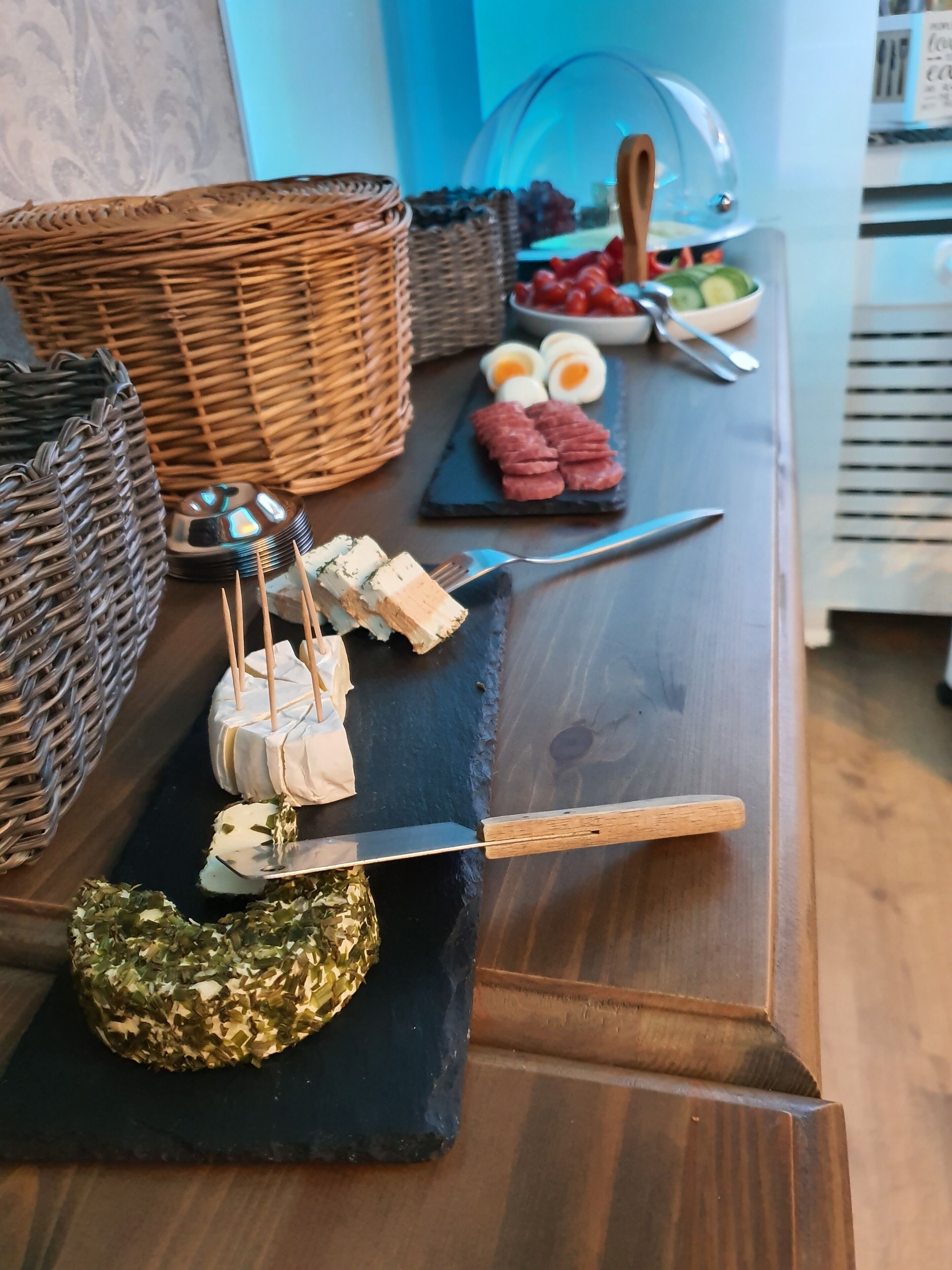 Ein Holztisch mit verschiedenen Speisen, darunter Käse, Fleisch und Gemüse, auf einer Schieferplatte angeordnet.