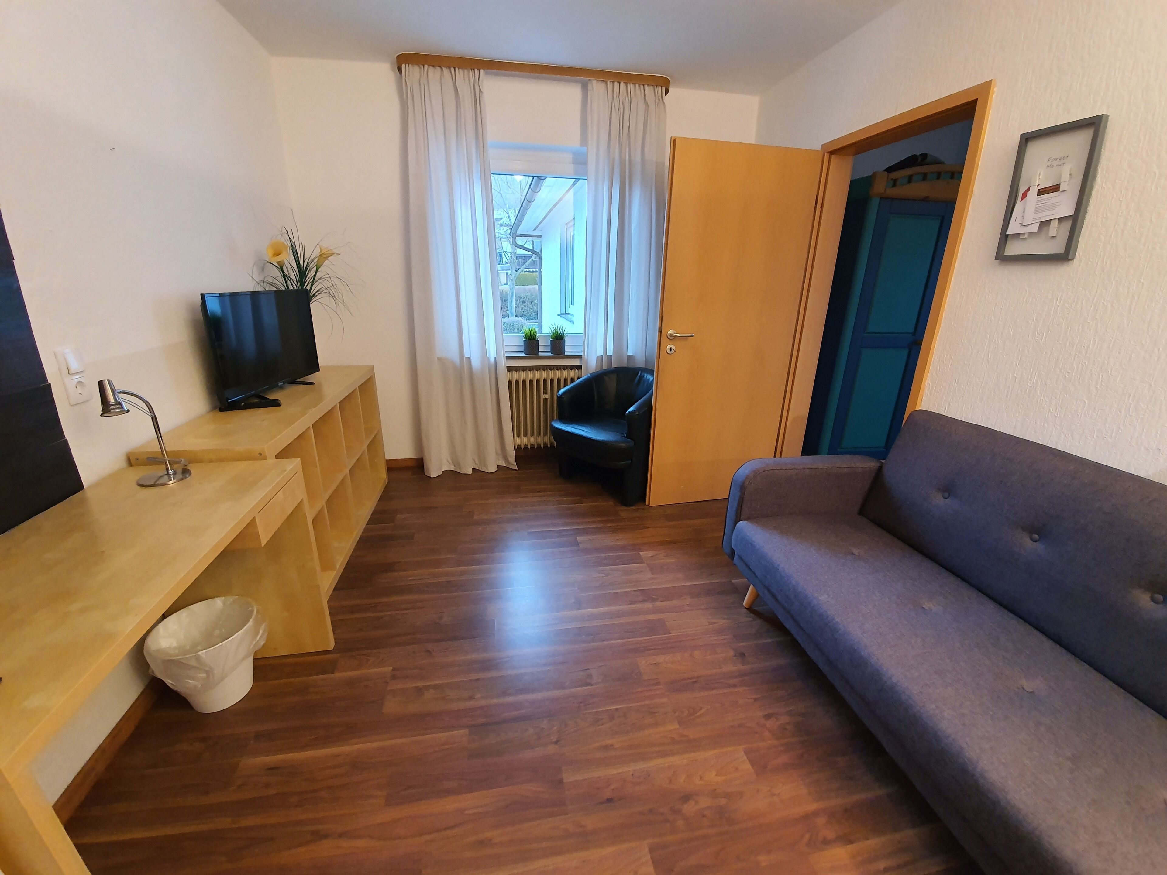 A compact living space with a wooden desk, a television, a sofa, and a radiator.