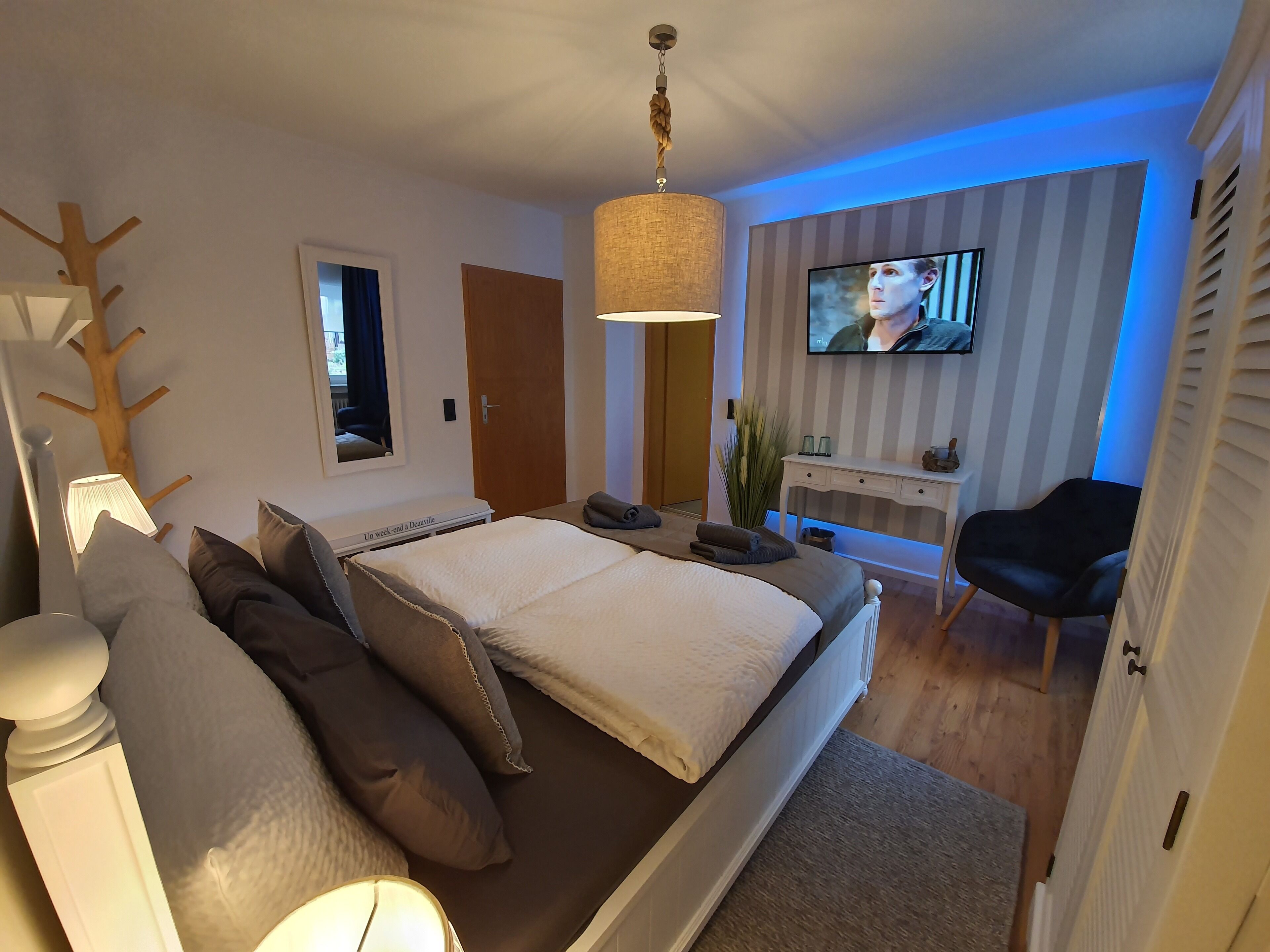 Et moderne soveværelse med en stor seng, et skrivebord, et fjernsyn og en plante.