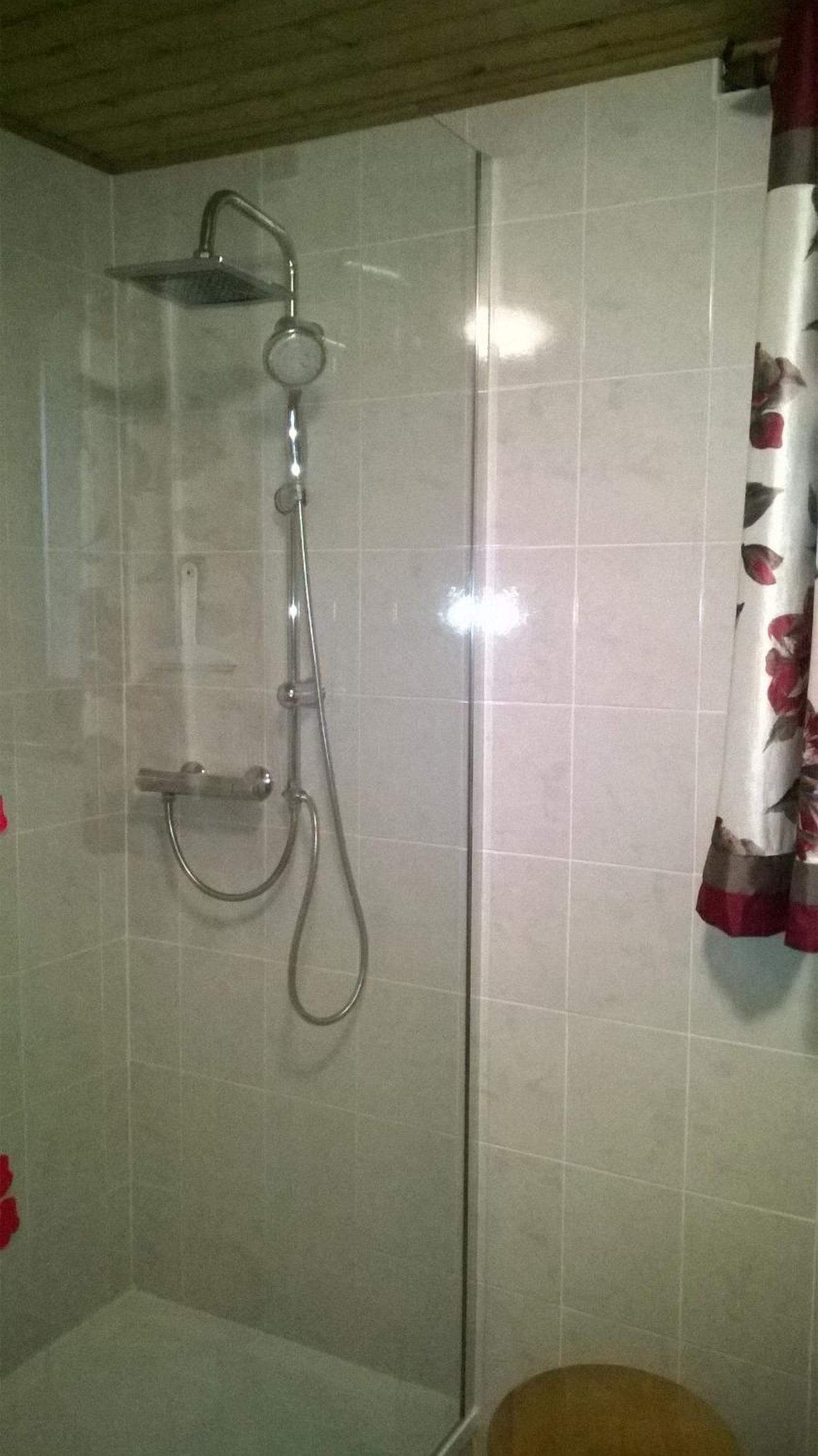 A shower area with a glass door, a handheld showerhead, and a wall-mounted faucet.