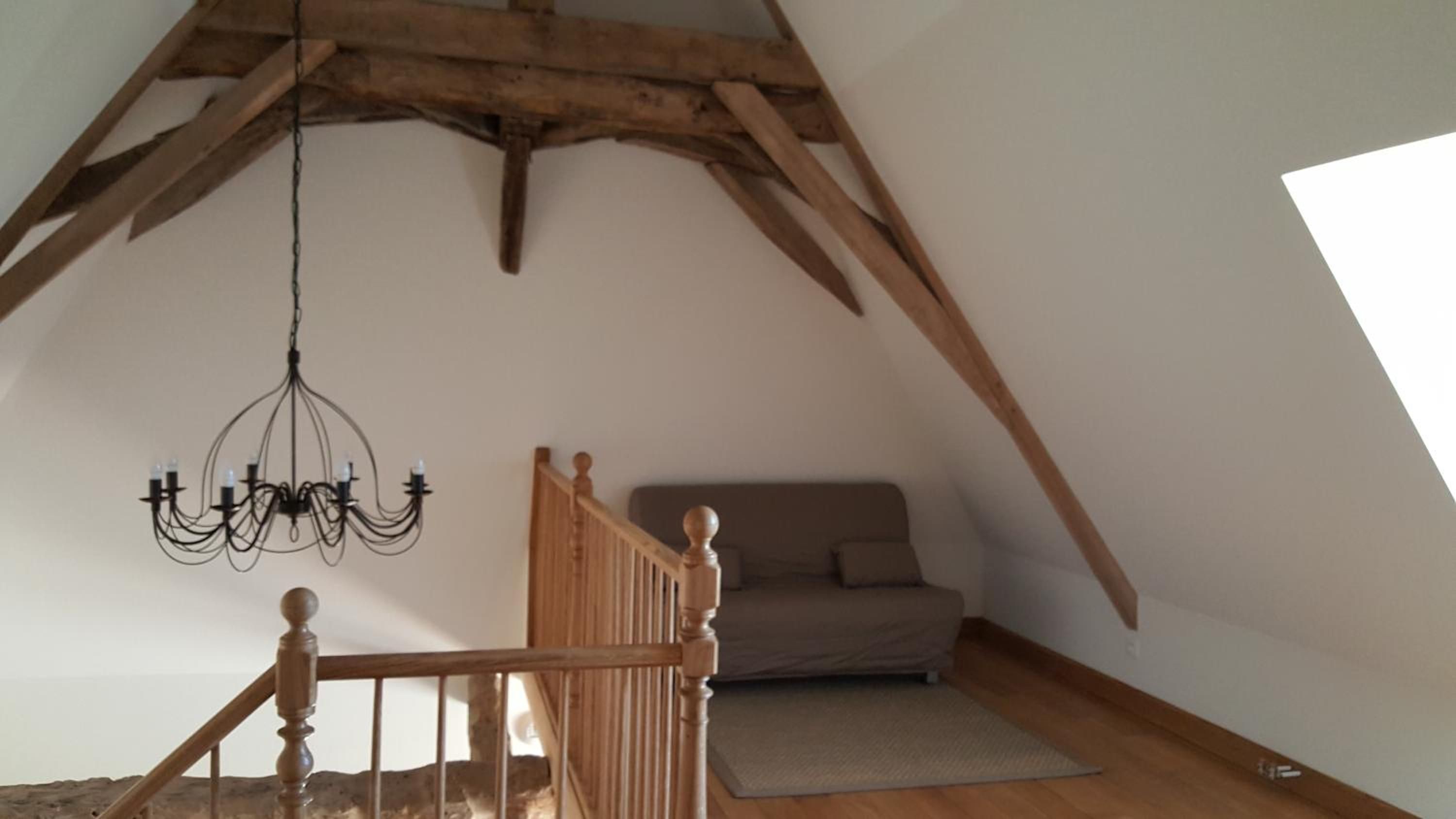 A loft bedroom with a sloped ceiling, a wooden staircase, a chandelier, a sofa, and a rug.