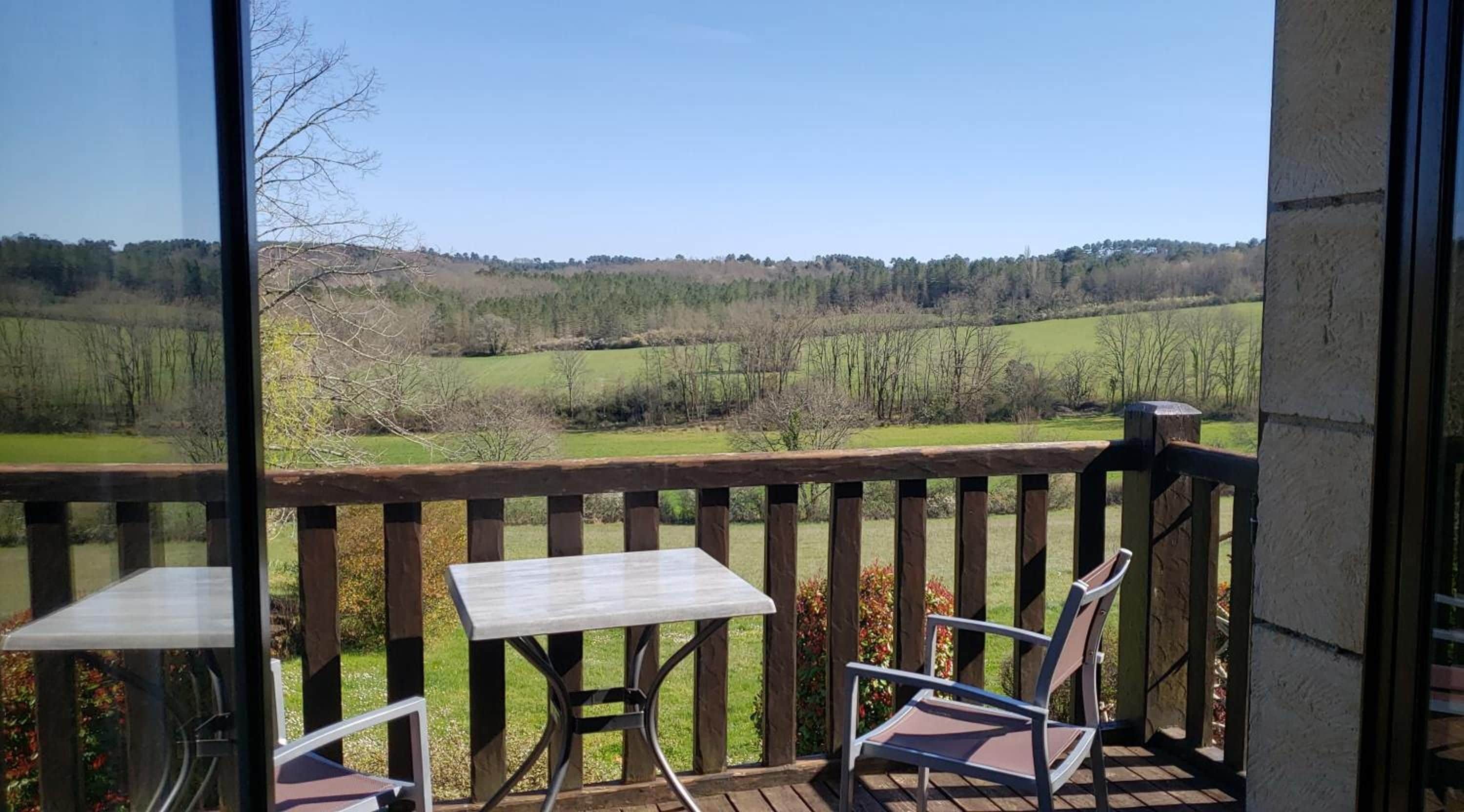 Een balkon met een tafel en stoelen, met uitzicht op een landelijk landschap met velden en bomen.