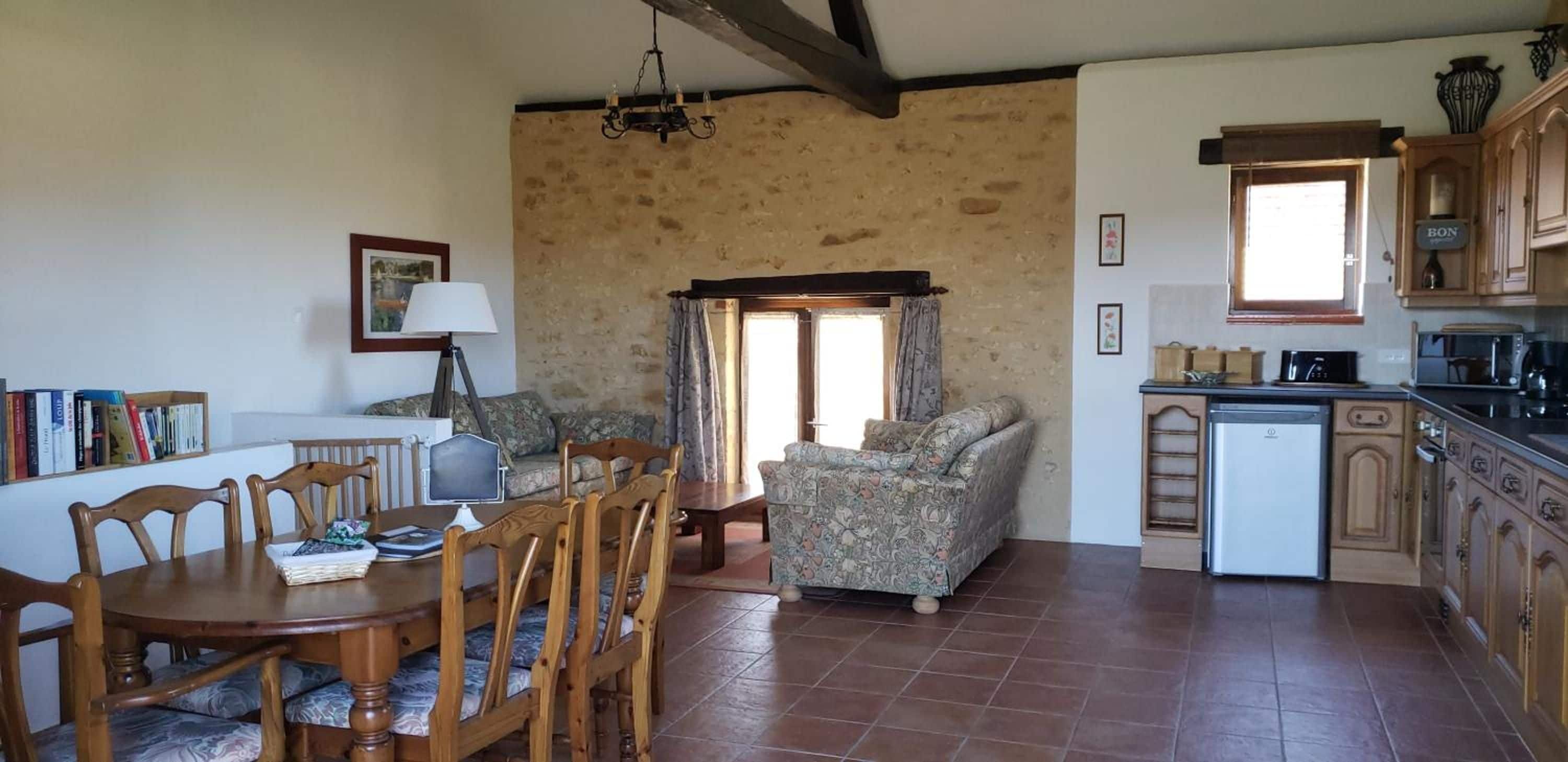 A cozy living room with a dining table, chairs, a sofa, and a kitchen area with cabinets and appliances.